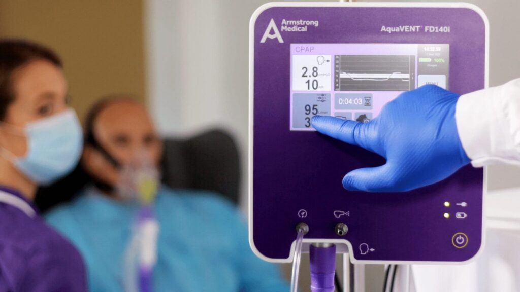 An AquaVENT FD140i with the litres per minute being highlighted with a hand, with a nurse and patient faded in the background
